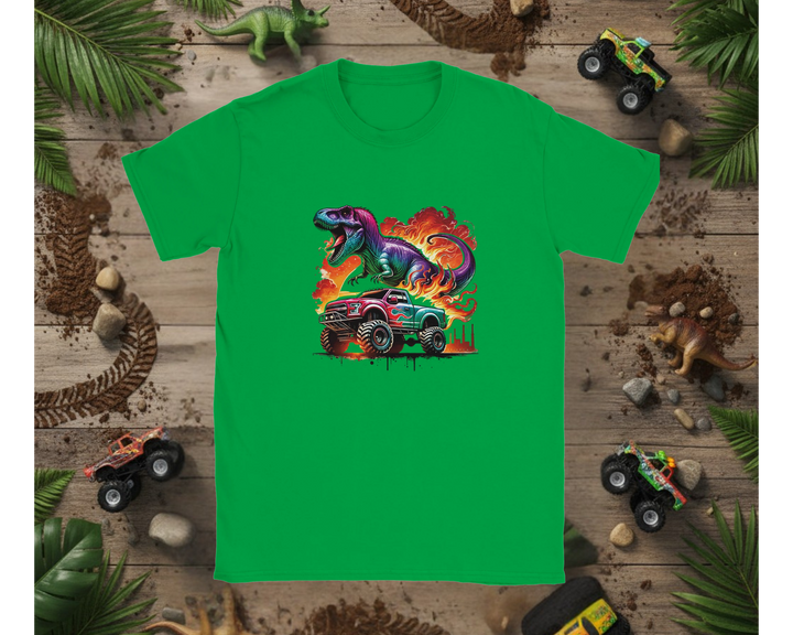 Green t-shirt with a colorful dinosaur and monster truck design on a wooden background with toy trucks and leaves.