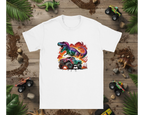 White t-shirt with colorful dinosaur and monster truck graphic on a wooden background with toy trucks and leaves.