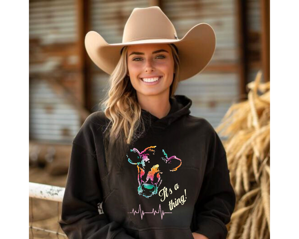 Woman wearing a black hoodie with colorful graphic and text, standing in a barn setting.