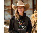Woman wearing a black hoodie with colorful graphic and text, standing in a barn setting.
