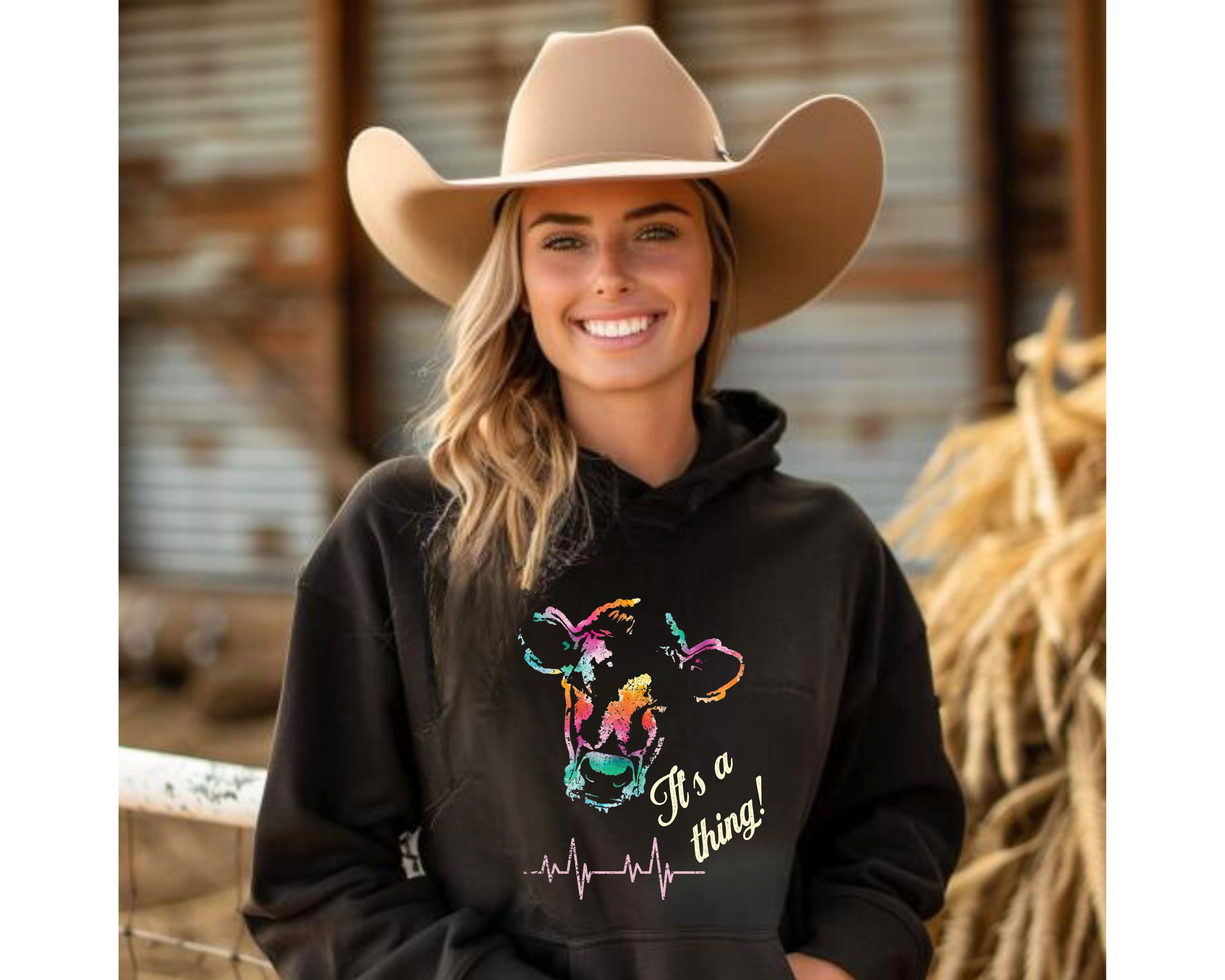 Woman wearing a black hoodie with colorful graphic and text, standing in a barn setting.