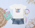 White t-shirt with colorful bull design, denim shorts, notebook, and accessories on a light blue background