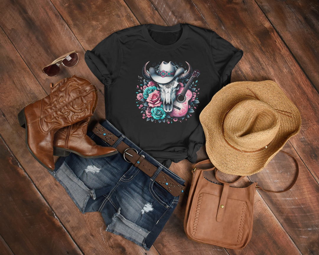 Black t-shirt with skull and floral design, cowboy boots, hat, and purse on wooden surface