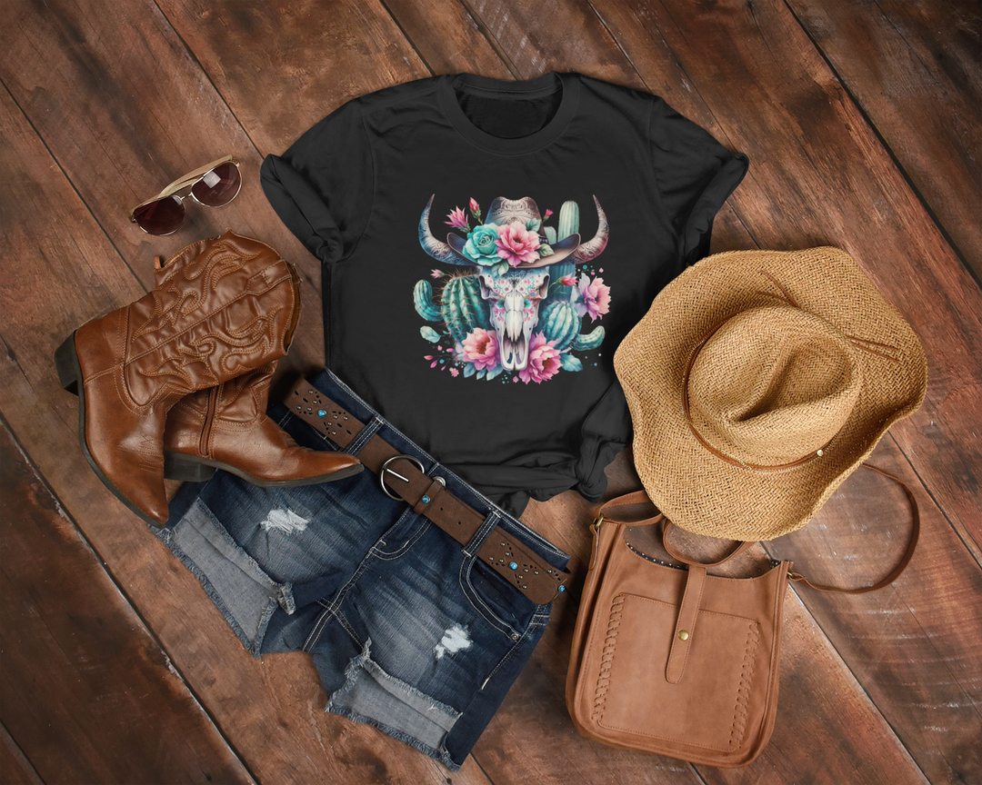 Black t-shirt with floral bull design, cowboy boots, hat, and purse on a wooden surface